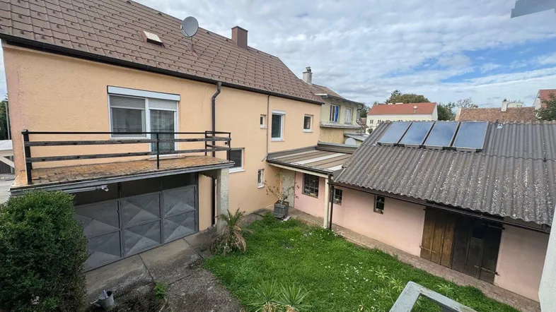 Blick auf den Hinterhof mit Rasenfläche, Garage und einem kleinen Balkon.