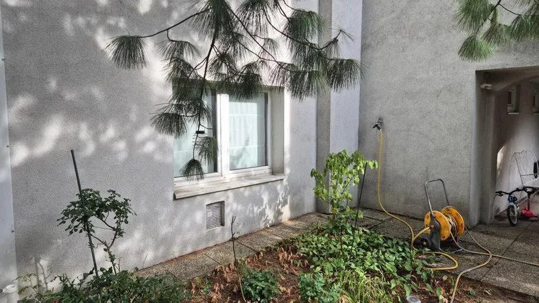 Außenbereich des Gebäudes mit einem kleinen Gartenbeet, Fenster und Bewässerungsschlauch.