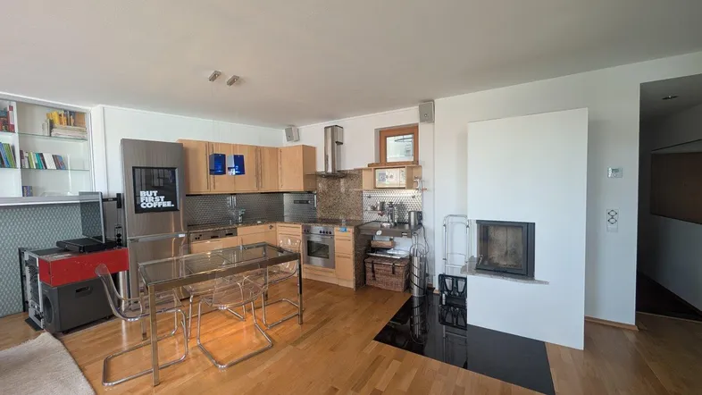 Heller offener Wohn-Essbereich mit integrierter Küche, Holzboden und modernem Kamin.