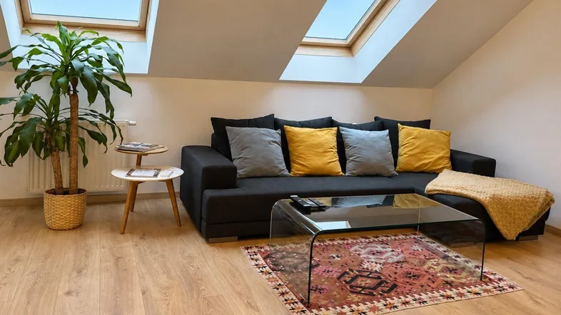 Gemütliches Wohnzimmer im Dachgeschoss mit bequemer Couch, Holzboden und Dachfenstern.