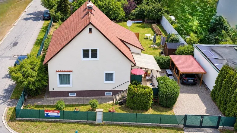Luftaufnahme eines Einfamilienhauses mit rotem Ziegeldach, Garten und Carport in ländlicher Umgebung.