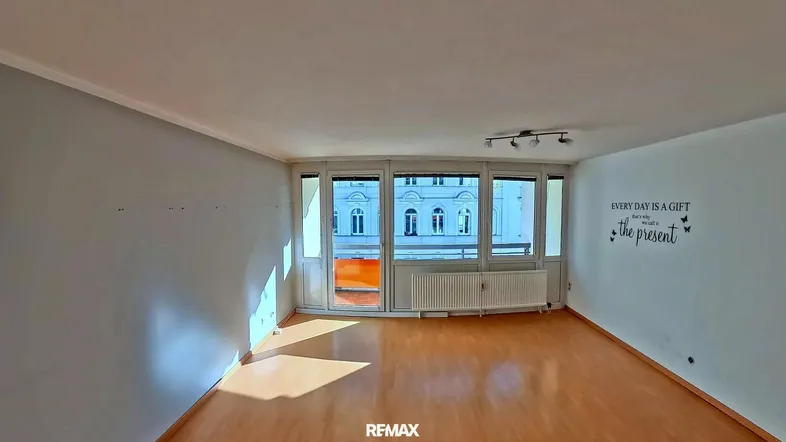 Helles Wohnzimmer mit Holzfußboden und großen Fenstern, die einen Blick auf die Straße ermöglichen.