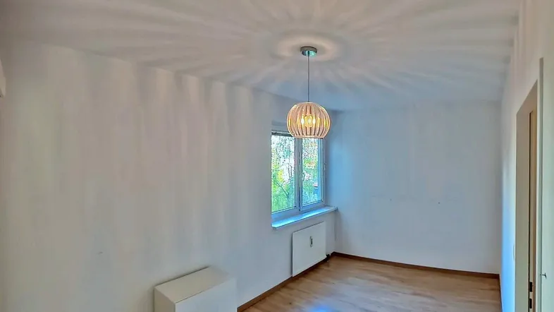 Helles Zimmer mit Holzfußboden und einem Fenster, das viel Tageslicht hereinlässt.