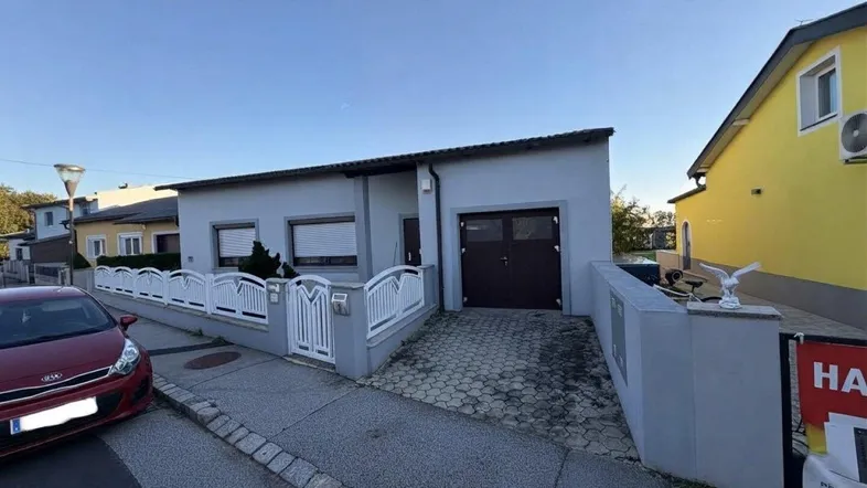 Einfamilienhaus mit Garage und Vorgarten, umgeben von einem Zaun.