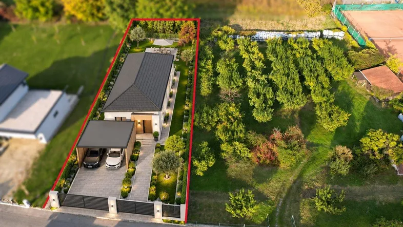 Luftaufnahme eines modernen Hauses mit Carport, gepflegtem Garten und angrenzendem Grundstück.