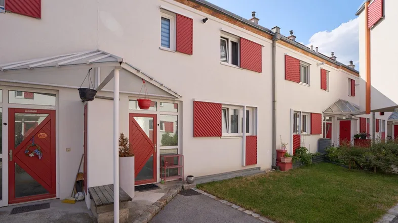 Reihenhäuser mit roten Fensterläden und kleinen Vorgärten in einer Wohnsiedlung.