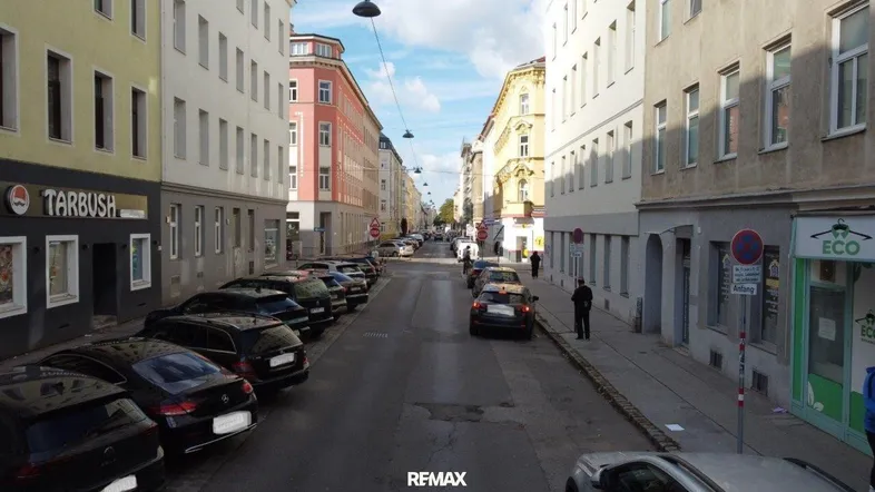 Eine belebte Straße mit parkenden Autos und mehrstöckigen Gebäuden in einer städtischen Umgebung.