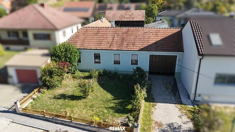 Luftaufnahme eines Einfamilienhauses mit Vorgarten und Garagenzufahrt in ländlicher Umgebung.