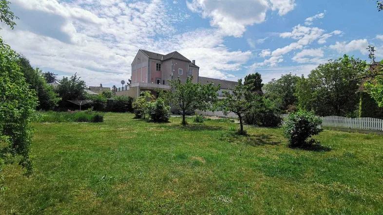 Großer Garten mit Rasenfläche und Blick auf das Haus unter blauem Himmel.