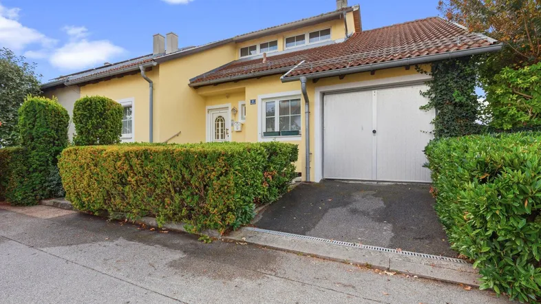 Gelbes Einfamilienhaus mit Garage, gepflegter Hecke und Vorgartenbereich.