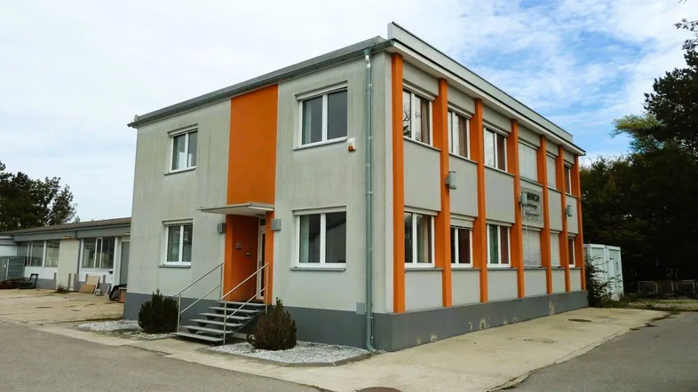 Ansicht eines zweistöckigen Geschäftsgebäudes mit grauer Fassade und orangefarbenen Akzenten unter blauem Himmel.
