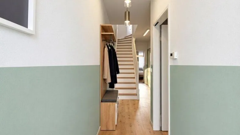Heller Eingangsbereich mit Holzfußboden, Garderobe und moderner Beleuchtung, der zum Treppenhaus führt.