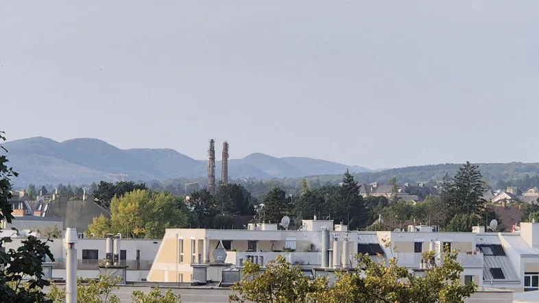 Weitblick über die Dächer der Stadt mit Bergen im Hintergrund und Industrieanlagen.