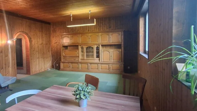 Rustikaler Wohn- und Essbereich mit Holzvertäfelung, grünem Teppichboden und einem großen Schrank.