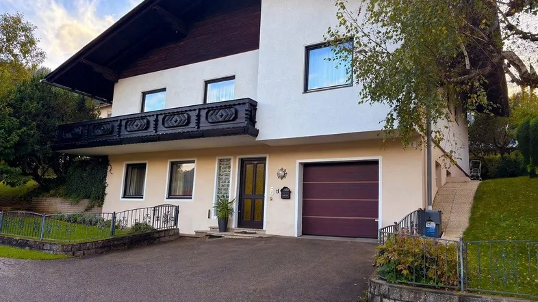 Traditionelles Haus mit Balkon, Garage und gepflegtem Vorgarten in ländlicher Umgebung.