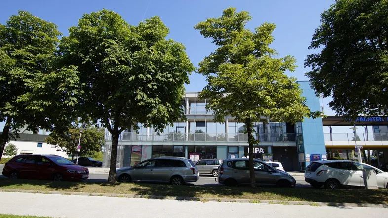 Moderne Geschäftsgebäude mit großen Glasfassaden und Bäumen entlang der Straße an einem sonnigen Tag.