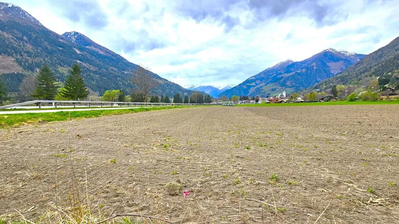 Weitläufiges Ackerland mit Blick auf die umliegende Berglandschaft und ein kleines Dorf in der Ferne.