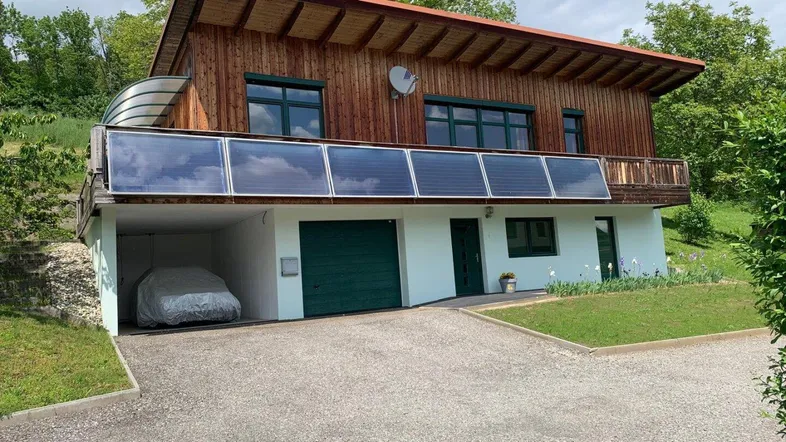Modernes Holzhaus mit Solarpaneelen, integrierter Garage und grüner Umgebung.
