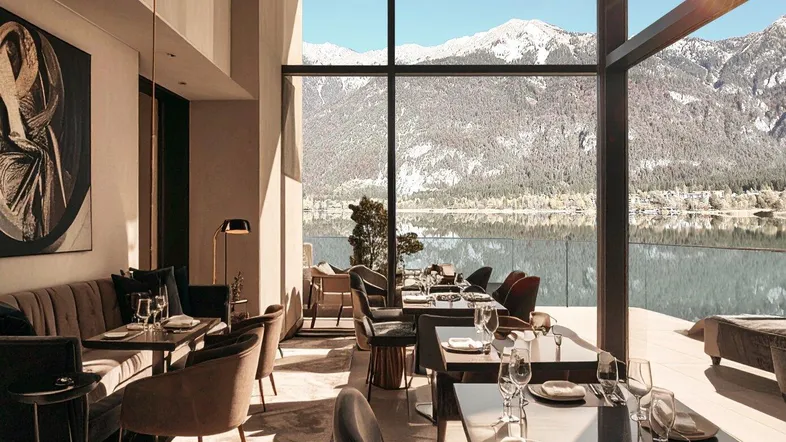 Elegantes Restaurant mit raumhohen Fenstern, die einen atemberaubenden Blick auf den See und die Berge bieten.