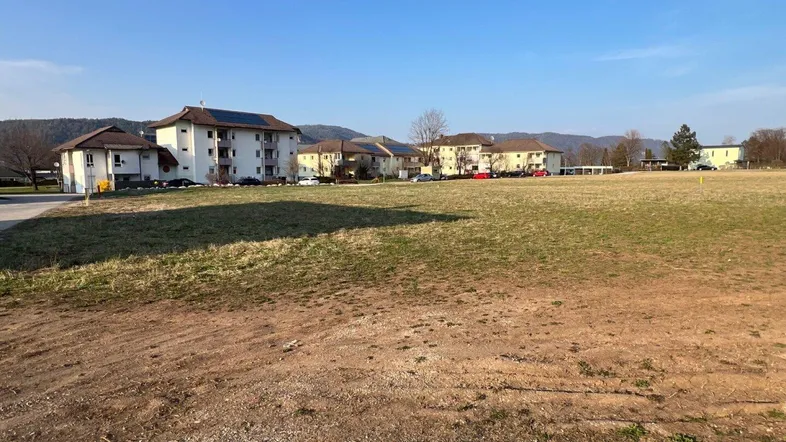 Weitläufiges unbebautes Grundstück mit Blick auf bestehende Wohngebäude und die umliegende Landschaft.