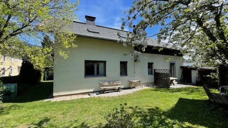 Hinteransicht des Hauses mit gepflegtem Garten und blühenden Bäumen unter blauem Himmel.