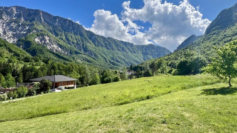 Idyllisches Haus in einer grünen Berglandschaft unter blauem Himmel mit weißen Wolken.