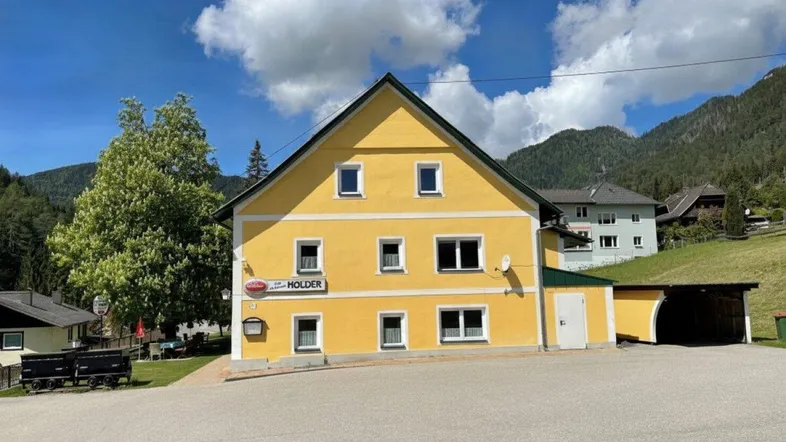 Gelbes Gebäude mit grünem Dach und Bergblick unter blauem Himmel.