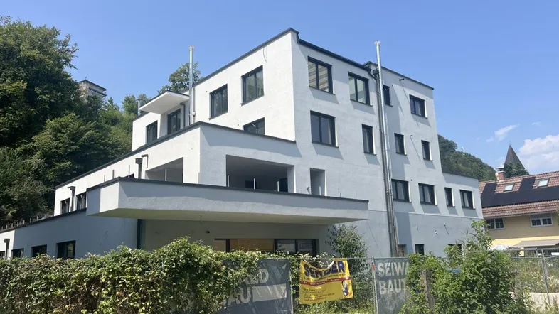 Moderner Neubau mit weißer Fassade, Flachdächern und Balkonen, umgeben von viel Grün.