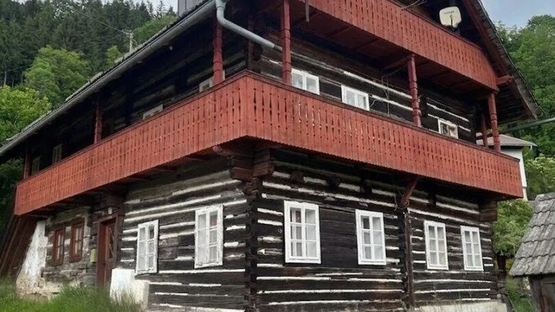 Traditionelles Holzhaus mit mehreren Balkonen und Satteldach in ländlicher Umgebung, umgeben von Bäumen.