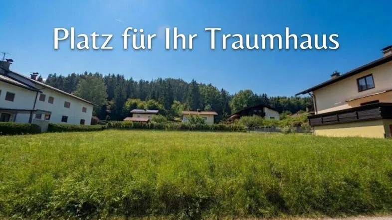 Grünes Baugrundstück mit umliegenden Häusern und Wald im Hintergrund, ideal für den Bau eines Traumhauses.