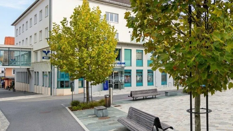 Modernes Gebäude mit öffentlichem Platz, Bänken und Bäumen in einer städtischen Umgebung.