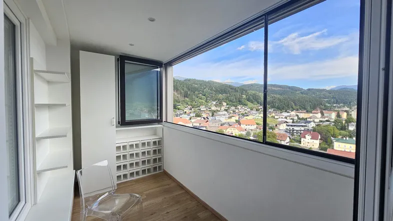 Helle Loggia mit großen Fenstern und weitem Blick über die Stadt und Berge.