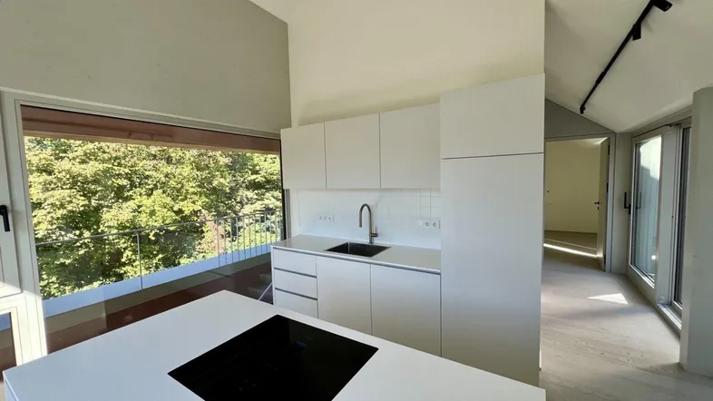 Moderne Küche mit weißer Kücheninsel, Induktionskochfeld und großem Fenster mit Blick ins Grüne.