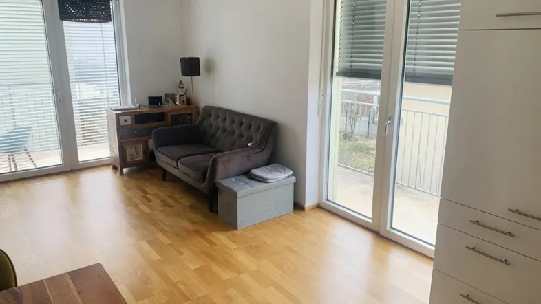 Helles Wohnzimmer mit Holzboden, Sofa und Zugang zu einem Balkon.