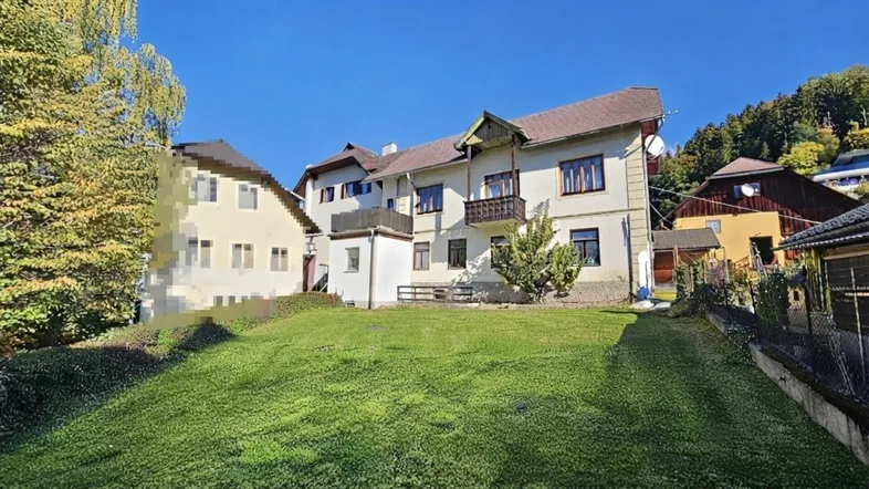 Großzügiger Rasenbereich vor einem traditionellen Gebäude mit mehreren Balkonen und Blick auf die umliegende Natur.