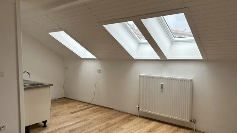 Heller Dachbodenraum mit schrägen Decken, Dachfenstern und Holzdielenboden, vorbereitet für eine Küchenzeile.