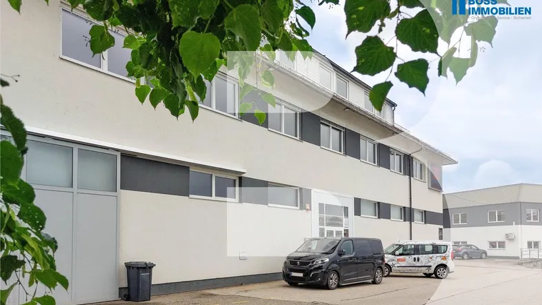 Außenansicht eines modernen Geschäftsgebäudes mit Parkplätzen und grüner Bepflanzung.