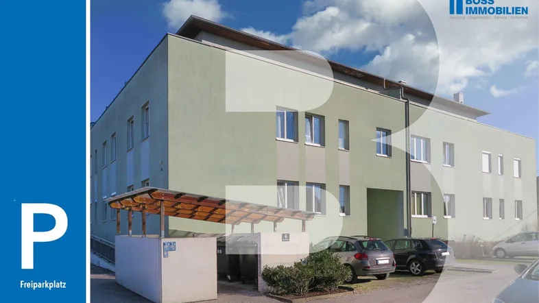 Gebäudeansicht mit Freiflächenparkplätzen und überdachtem Stellplatz unter blauem Himmel.