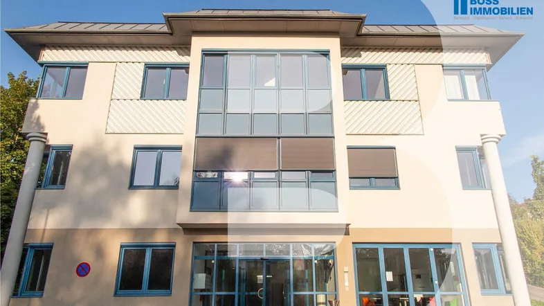 Moderne Gebäudefassade mit großen Fenstern und blauen Rahmen unter klarem Himmel.
