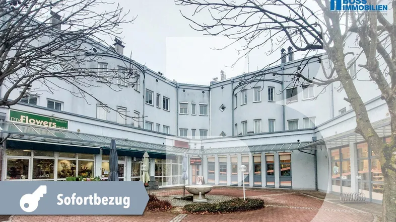 Außenansicht eines Gebäudes mit Geschäften und einem gepflasterten Innenhof mit Brunnen.