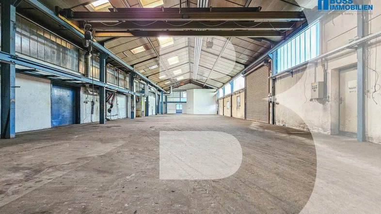 Geräumige Lagerhalle mit hoher Decke, Oberlichtern und Betonboden, ideal für industrielle Nutzung.
