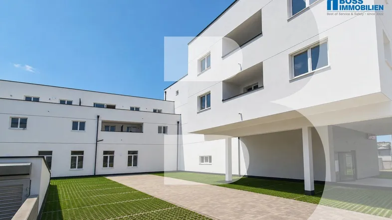 Moderne weiße Wohngebäude mit Balkonen, Carport und gepflasterter Zufahrt mit Rasengittersteinen.