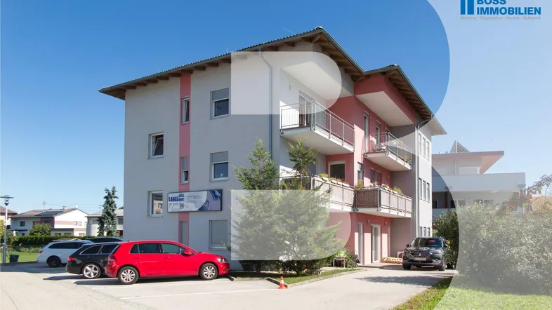 Modernes Mehrfamilienhaus mit mehreren Balkonen und Parkplätzen im Freien unter blauem Himmel.
