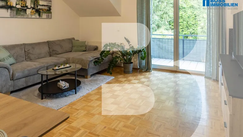 Helles Wohnzimmer mit gemütlichem Sofa, Parkettboden und Zugang zu einem Balkon mit Grünblick.