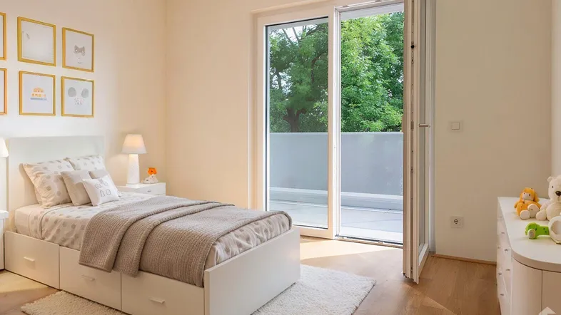Helles Schlafzimmer mit Holzboden, Bett mit Stauraum und Zugang zu einem Balkon mit Grünblick.