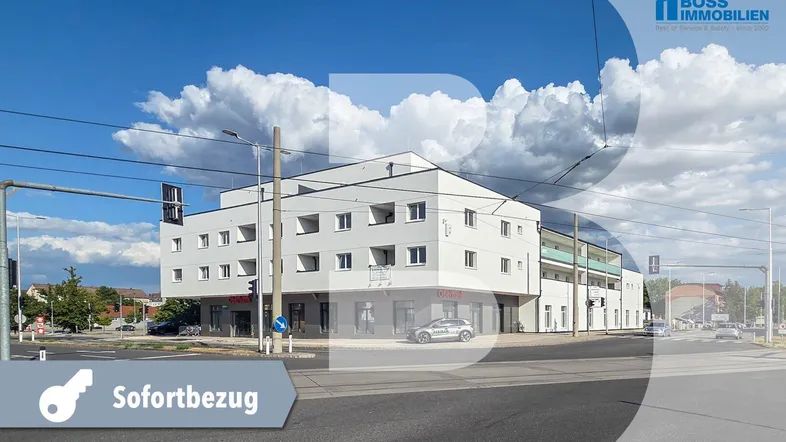 Modernes weißes Gebäude an einer Straßenkreuzung mit blauen Balkonen und klarem Himmel.