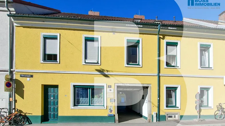 Gelbes Mehrfamilienhaus mit grünen Fensterrahmen und Garageneinfahrt an einer Straße gelegen.