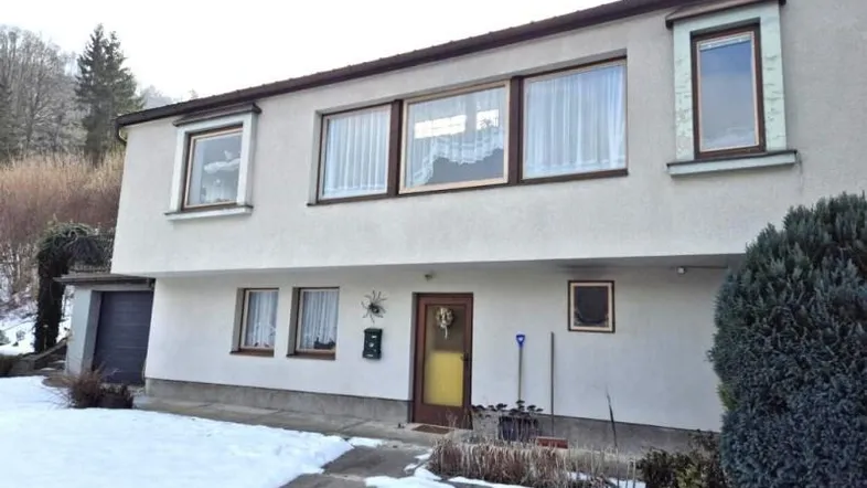 Vorderansicht eines Hauses mit heller Fassade, braunen Fenstern und verschneitem Vorgarten.