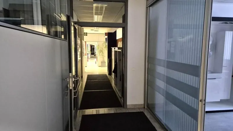 Heller Bürogang mit modernen Glaswänden und Türen, der zu weiteren Büroräumen führt.