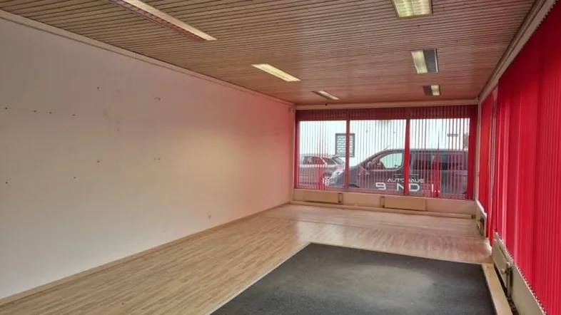 Geräumiger Gewerberaum mit großen Fenstern, Holzdecke und rotem Lamellenvorhang, ideal für Ausstellungszwecke.